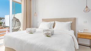 A hotel room with a large bed, white bedding, a wooden nightstand, and a view of the sea. - Omnia Mykonos Boutique Hotel & Suites (Mykonos)