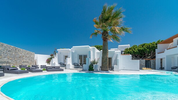 A modern pool area with white buildings, palm trees, and outdoor seating. - Omnia Mykonos Boutique Hotel & Suites (Mykonos)