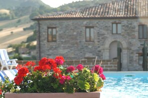 A stone building with a pool in the foreground and a mountainous landscape in the background. - Agriturismo Il Boschetto (Arcevia)