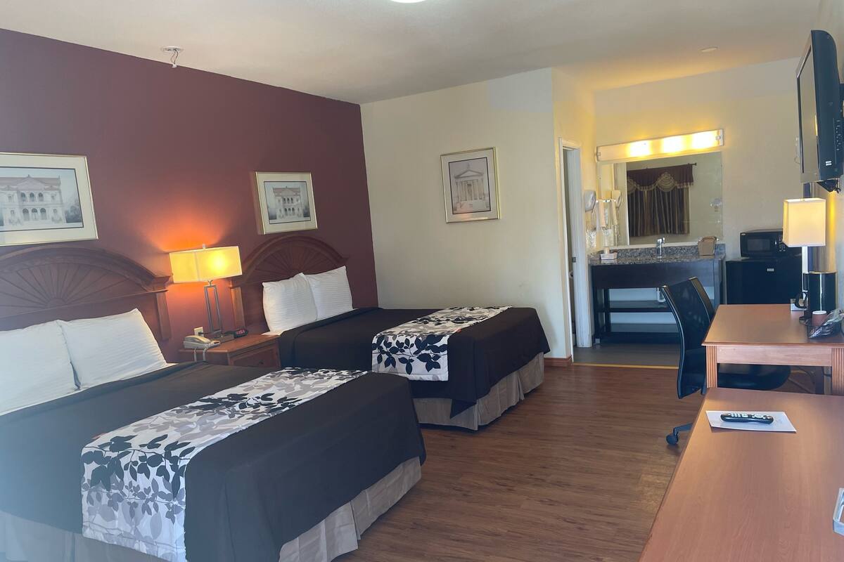 Habitación de hotel con dos camas, un escritorio, una silla, microondas, teléfono y una pequeña cocina.