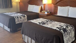 A hotel room with two beds, a wooden headboard, a nightstand with a lamp, and framed pictures on the wall.