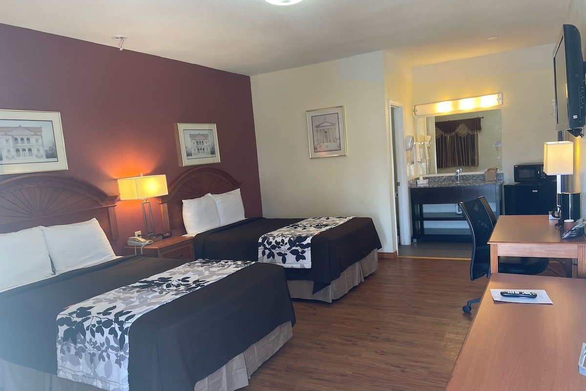 Habitación de hotel con dos camas, un escritorio, una silla, microondas, teléfono y espejo.