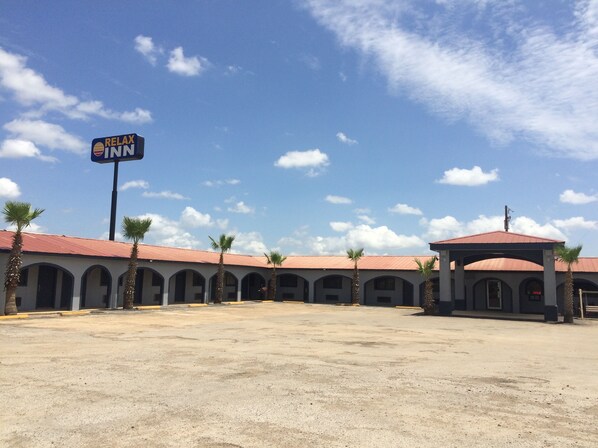 A motel with a red roof and multiple arched windows, a signboard, and palm trees in front.