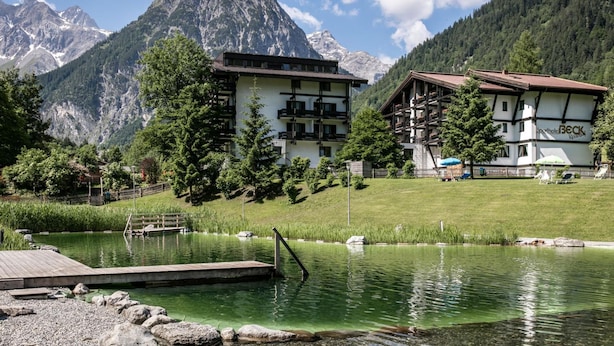 A mountain resort with a lake, wooden buildings, and a mountain backdrop. - Sporthotel Beck (Brand)