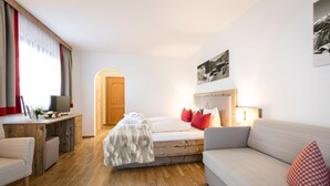 A bedroom with a bed, a desk, a sofa, and a wooden door. - Sporthotel Beck (Brand)