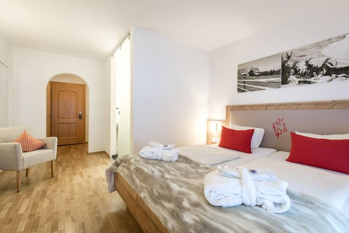 A hotel room with a bed, a chair, a wooden door, and a wall-mounted picture.