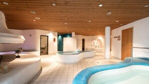 A spa area with a large indoor pool, a hot tub, and a seating area with a bird sculpture. - Sporthotel Beck (Brand)