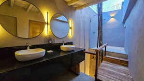 A modern bathroom with two round mirrors, a black countertop, and a wooden staircase leading to an outdoor area.