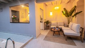 A modern living room with a sofa, coffee table, and a large plant. There is a mirror on the wall and a staircase leading to another room.