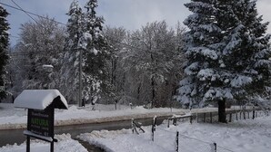A snow-covered landscape with a sign for 'Guesthouse Natura' near a stream. - Natura Plitvice Lakes (Plitvicka Jezera)