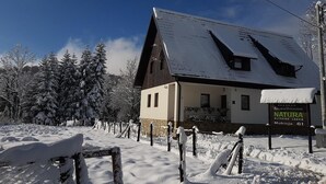 A guesthouse named Natura with a sloped roof, surrounded by snow-covered trees and a fence. - Natura Plitvice Lakes (Plitvicka Jezera)