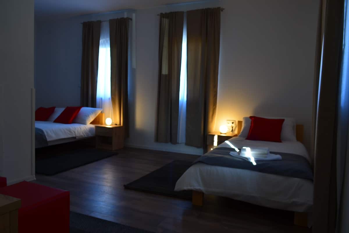 A hotel room with two beds, a small table, and a window with curtains.