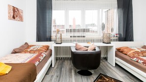 Ein modernes Zimmer mit einem Bett, einem Schreibtisch und einem Stuhl. Es gibt ein Fenster mit Vorhängen, eine Heizung und Blick auf die Stadt.
