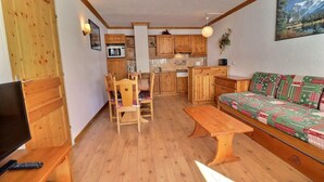 A cozy living room with a wooden floor, a sofa, a dining table with chairs, a kitchen area with wooden cabinets, and a TV. - 10m from ski slopes, Ground floor, balcony, 40m², Méribel-Mottaret (Méribel - Les Allues)