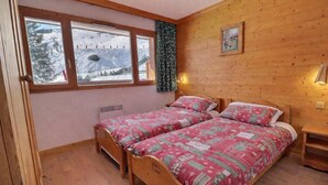 A room with two wooden beds, a window with a view of a snowy landscape, a radiator, and a small bedside table. - 10m from ski slopes, Ground floor, balcony, 40m², Méribel-Mottaret (Méribel - Les Allues)