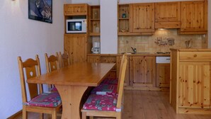 A wooden dining table with chairs, a microwave, and a sink in a kitchen with wooden cabinets. - 10m from ski slopes, Ground floor, balcony, 40m², Méribel-Mottaret (Méribel - Les Allues)