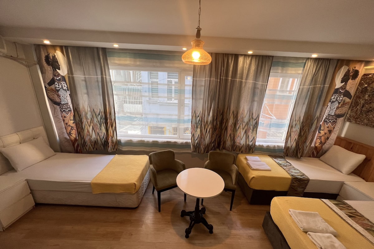 A modern hotel room with a sofa bed, a small round table, and a single bed.