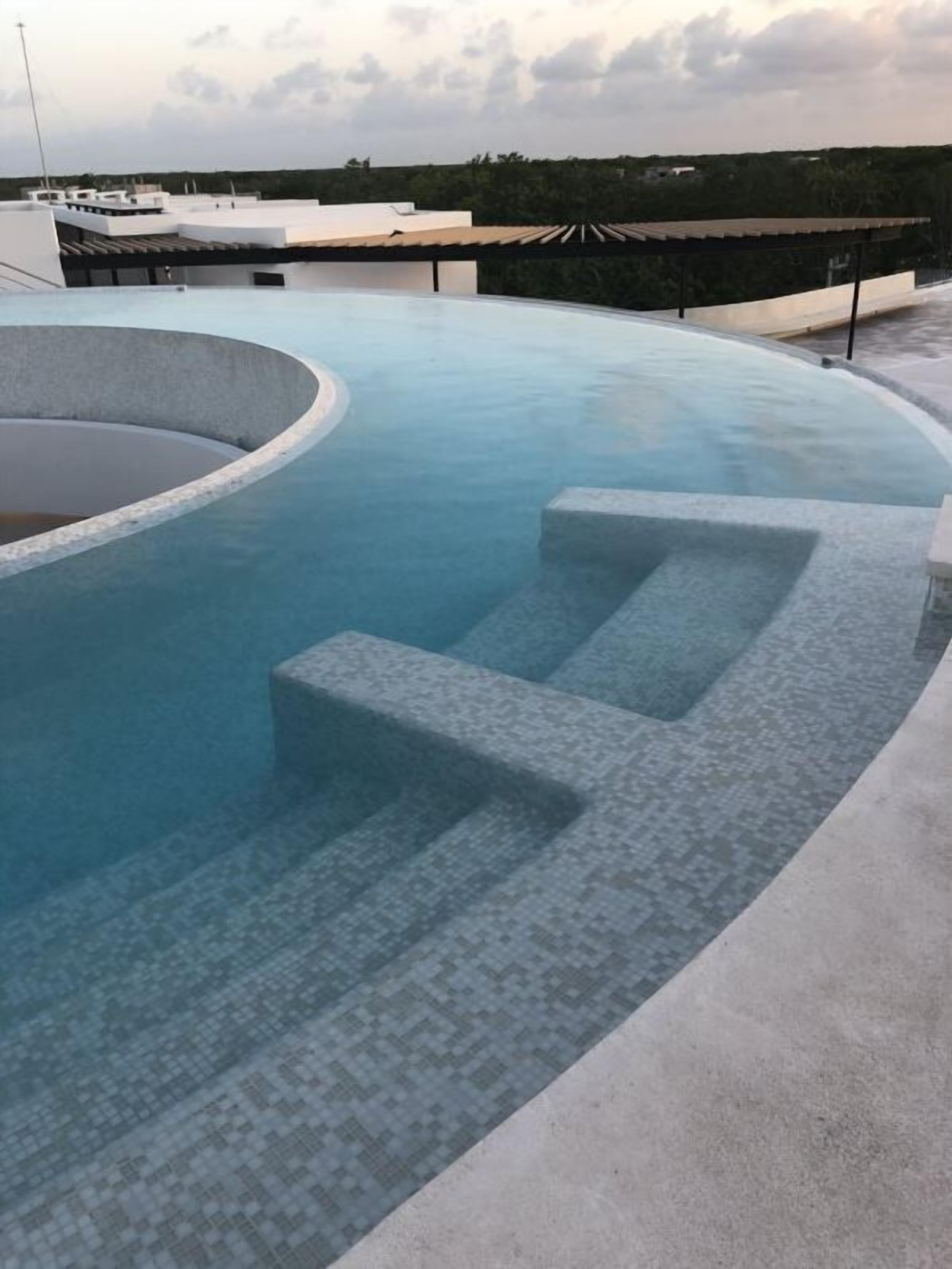 A rooftop pool with a circular design, steps leading into the water, and a view of the surrounding area.