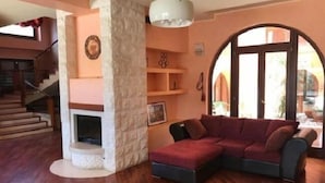 Uma sala de estar com lareira de pedra, um sofá seccional vermelho e escada que leva a um andar superior.