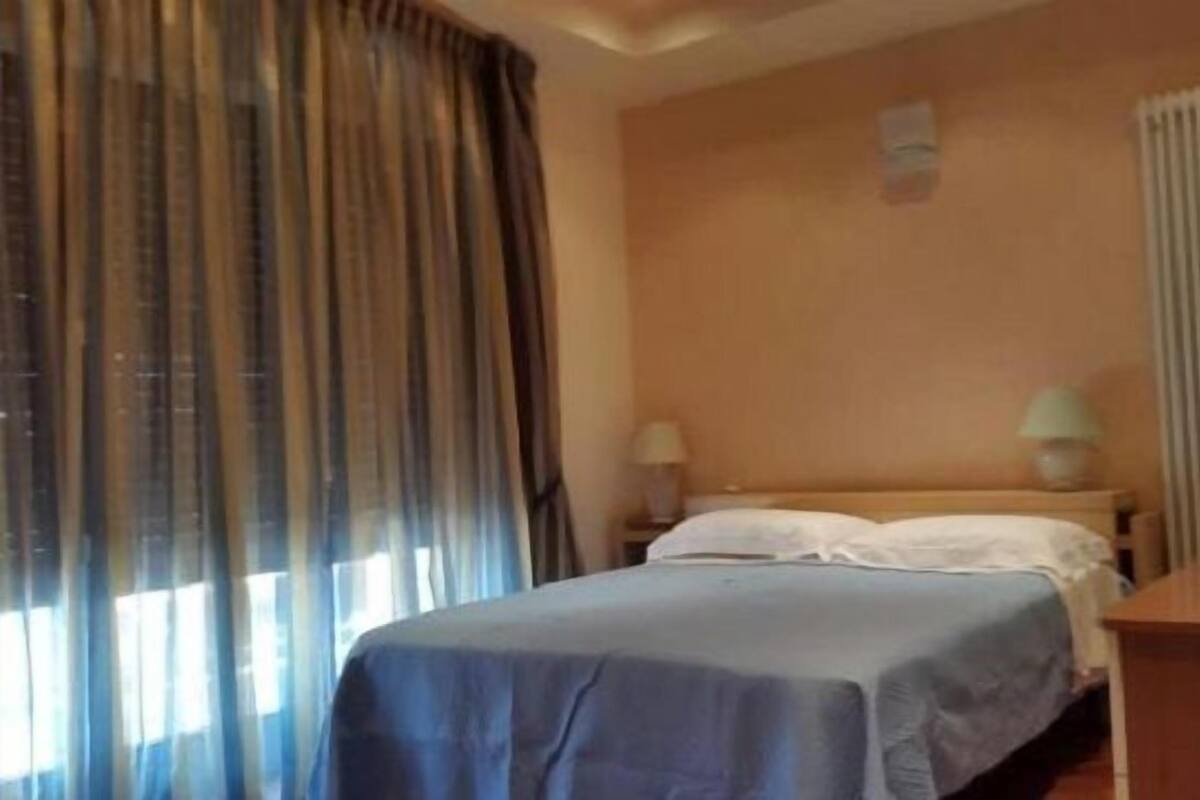 Ein Hotelzimmer mit Bett, Nachttisch, Lampe und einem Fenster mit Vorhängen.