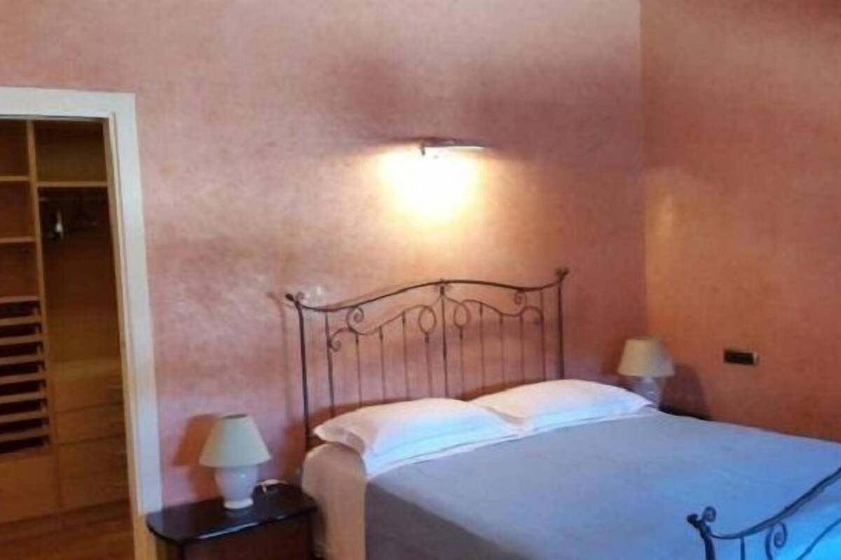 Ein Schlafzimmer mit einem Metallbettgestell, einem Nachttisch mit Lampe und einem Schrank mit vielen Ablagen.