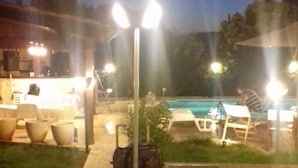 Área de piscina externa com piso de pedra, espreguiçadeiras e um caminho bem iluminado.