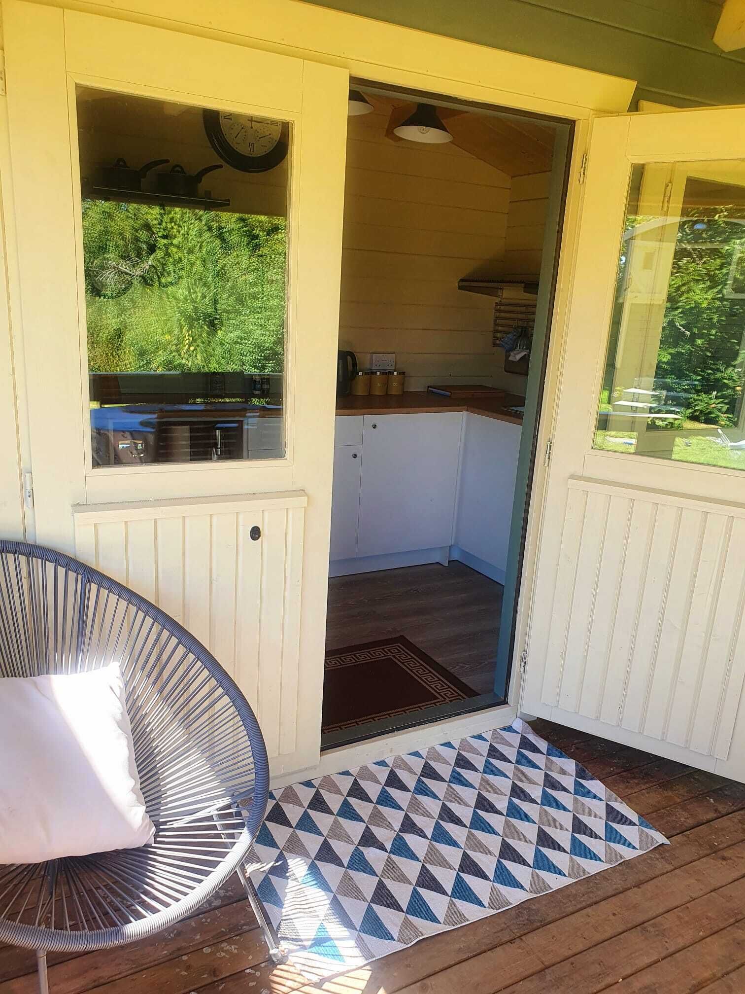 Un espacio exterior cubierto con una silla, un tapete estampado y vistas a una cocina a través de una puerta abierta.