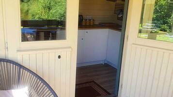 Un espacio exterior cubierto con una silla, un tapete estampado y vistas a una cocina a través de una puerta abierta.