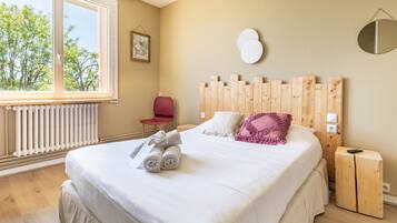 Ein Schlafzimmer mit großem Fenster, einem Holzkopfteil, einem Bett mit weißer Bettwäsche, einem roten Sessel und einem kleinen Nachttisch.