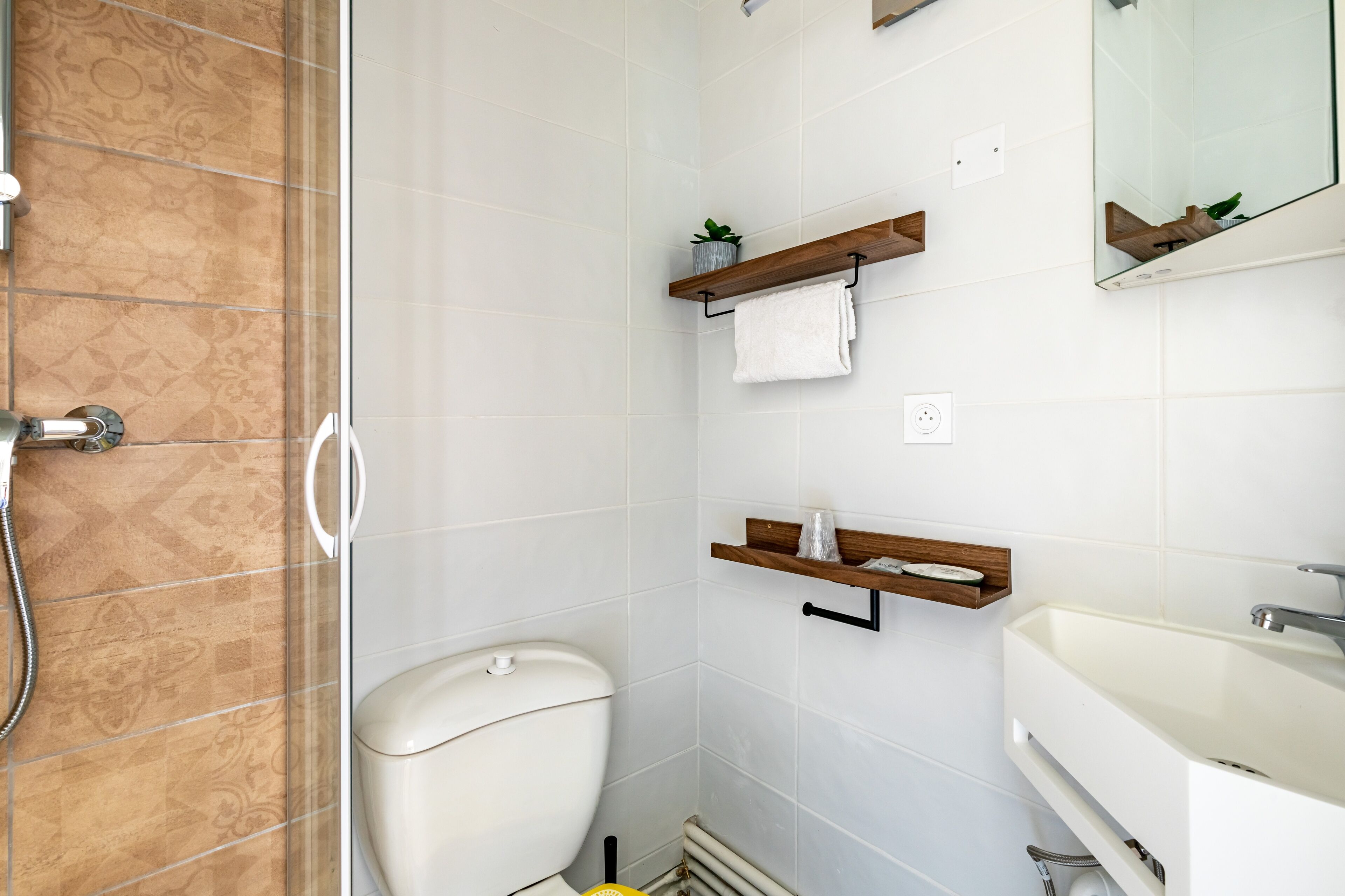Un baño con inodoro, ducha y lavabo. Hay repisas de madera con toallas y una planta pequeña.