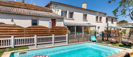 Una piscina rectangular con borde de madera, un flotador inflable en el agua y una valla blanca.