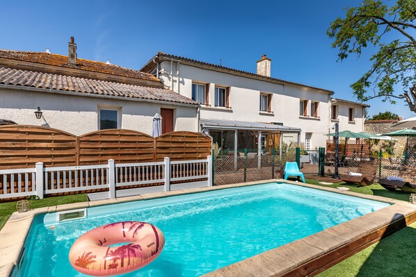 A rectangular swimming pool with a wooden deck edge, a floating inflatable pool float, and a white fence. - Hotel les vieux Acacias (Queyrac)