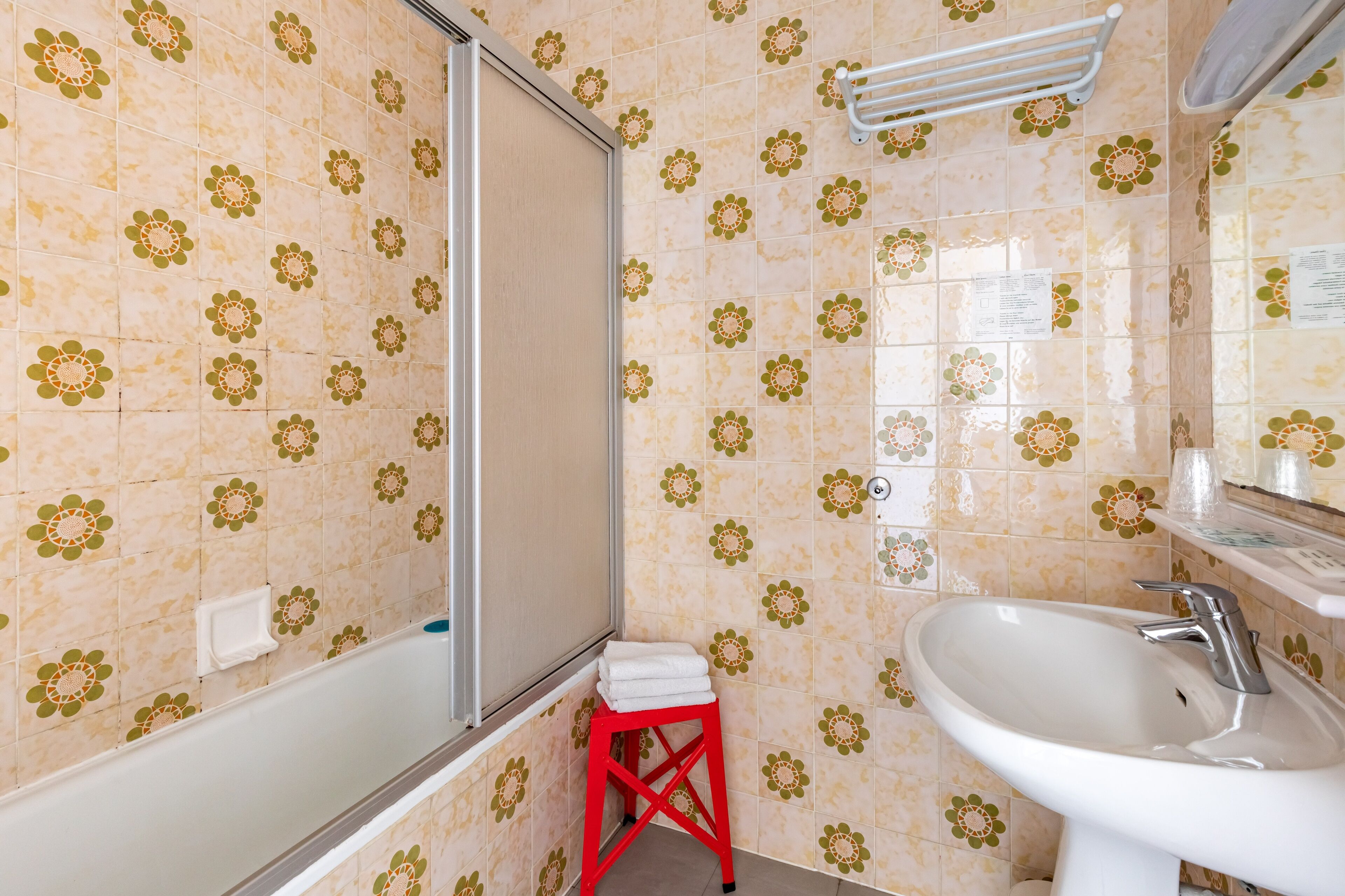A bathroom with a shower, a sink, and a red stool.