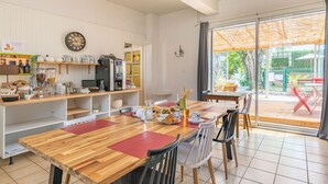 A spacious kitchen with a wooden table and chairs, equipped with various appliances and a large window offering a view of the outdoors. - Hotel les vieux Acacias (Queyrac)