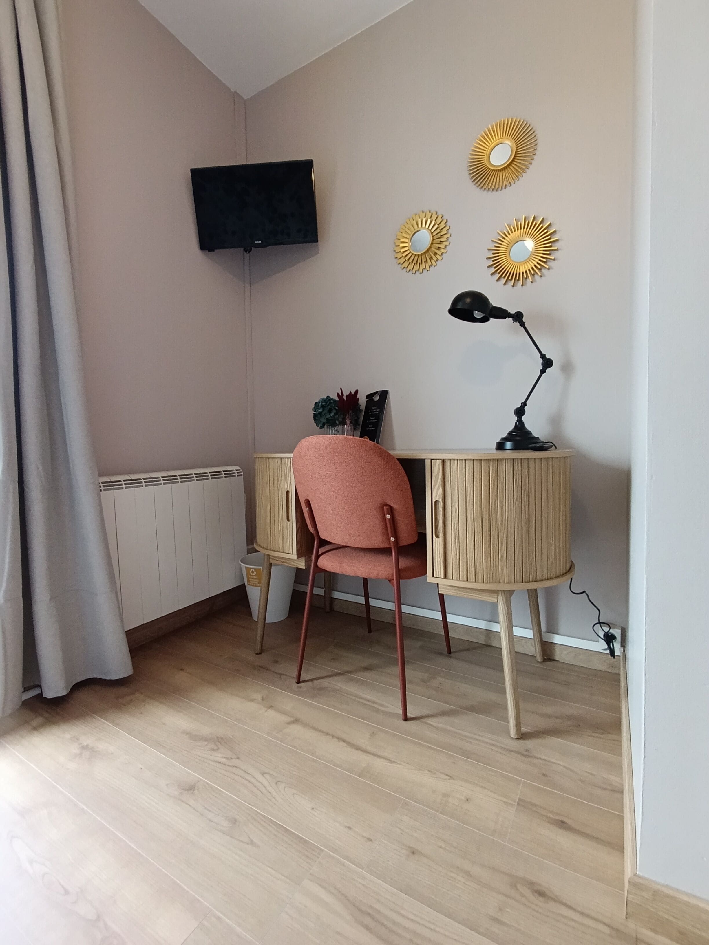 A room with a wooden desk, a red chair, a black lamp, and decorative sunburst mirrors on the wall.