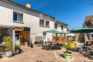 A courtyard with outdoor seating, potted plants, and a reception sign for a hotel. - Hotel les vieux Acacias (Queyrac)
