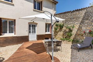 Une terrasse avec une plateforme en bois, une table et des chaises, un transat et un parasol blanc.