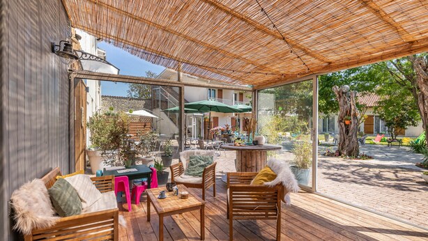 A covered patio area with wooden furniture, a table, and chairs. - Hotel les vieux Acacias (Queyrac)