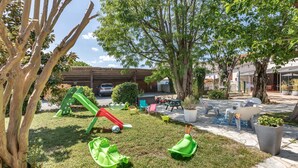 A children's play area with a slide and various toys, surrounded by trees and outdoor seating. - Hotel les vieux Acacias (Queyrac)