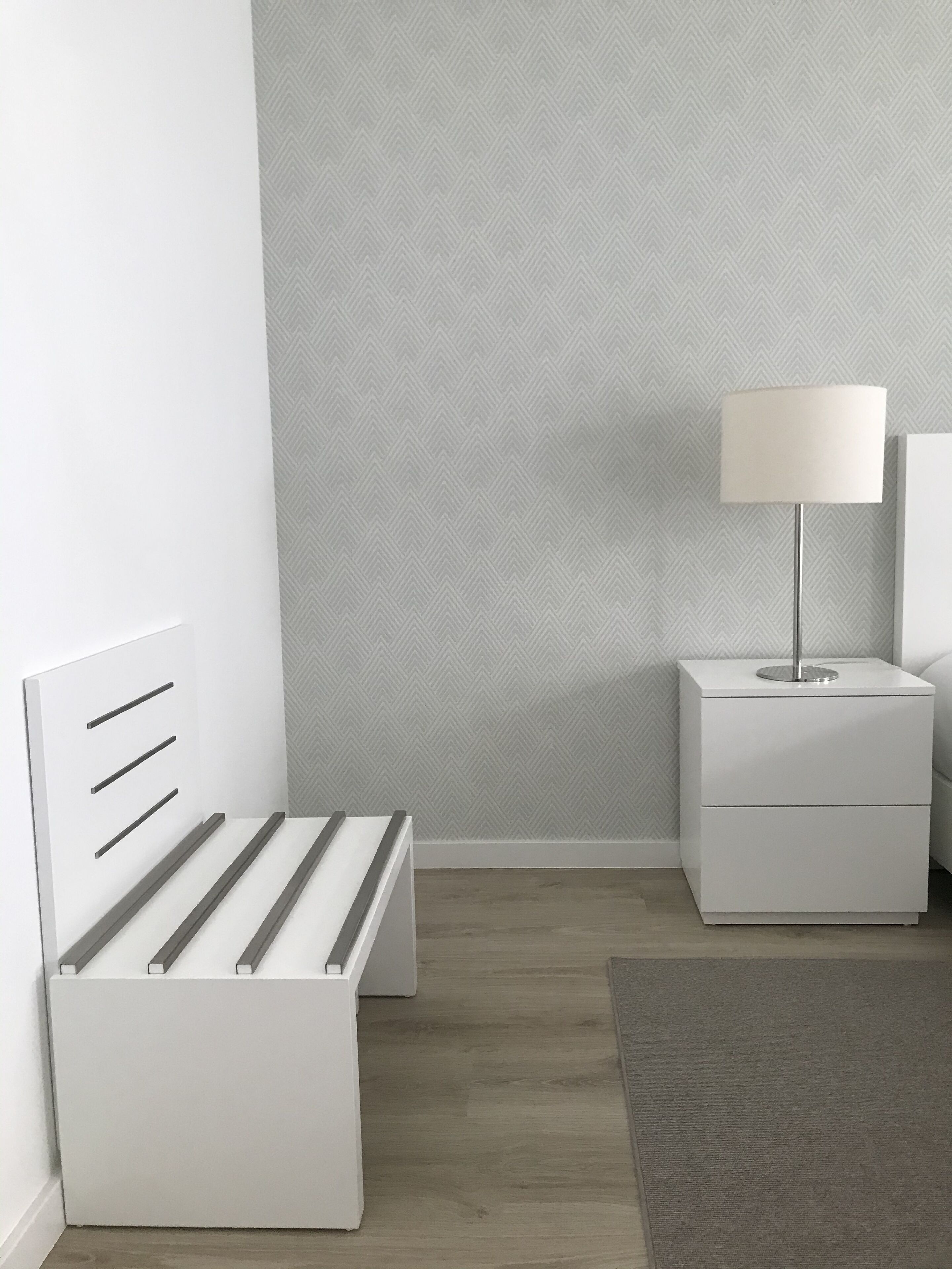 A minimalist bedroom with a white bed, a bedside table with a lamp, and a nightstand.