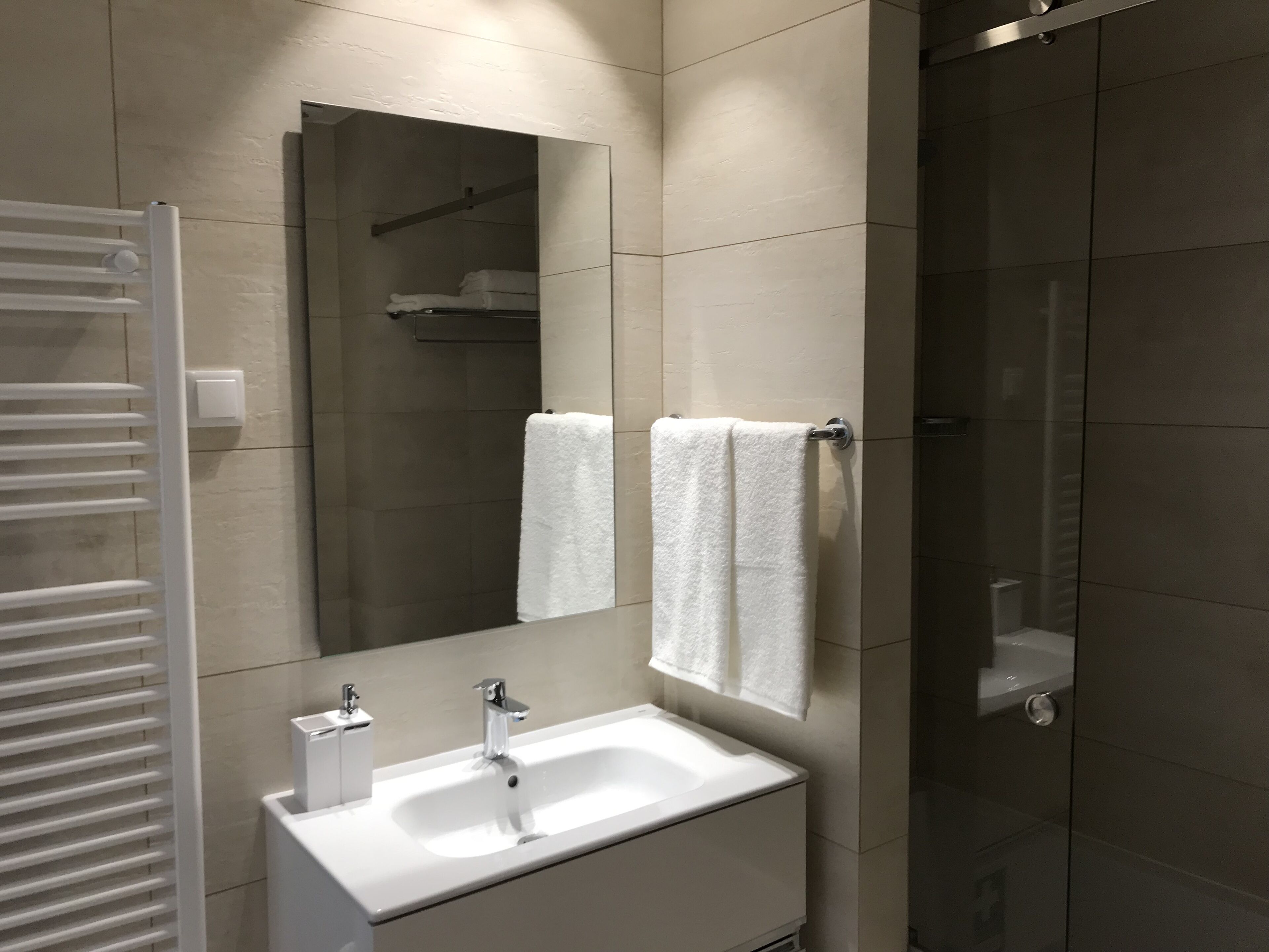 A modern bathroom with a white sink, two faucets, a mirror, and a towel rack.