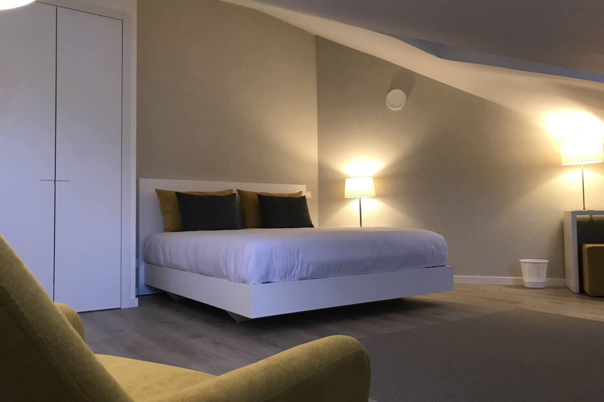 A modern bedroom with a bed, bedside lamps, and a sofa.