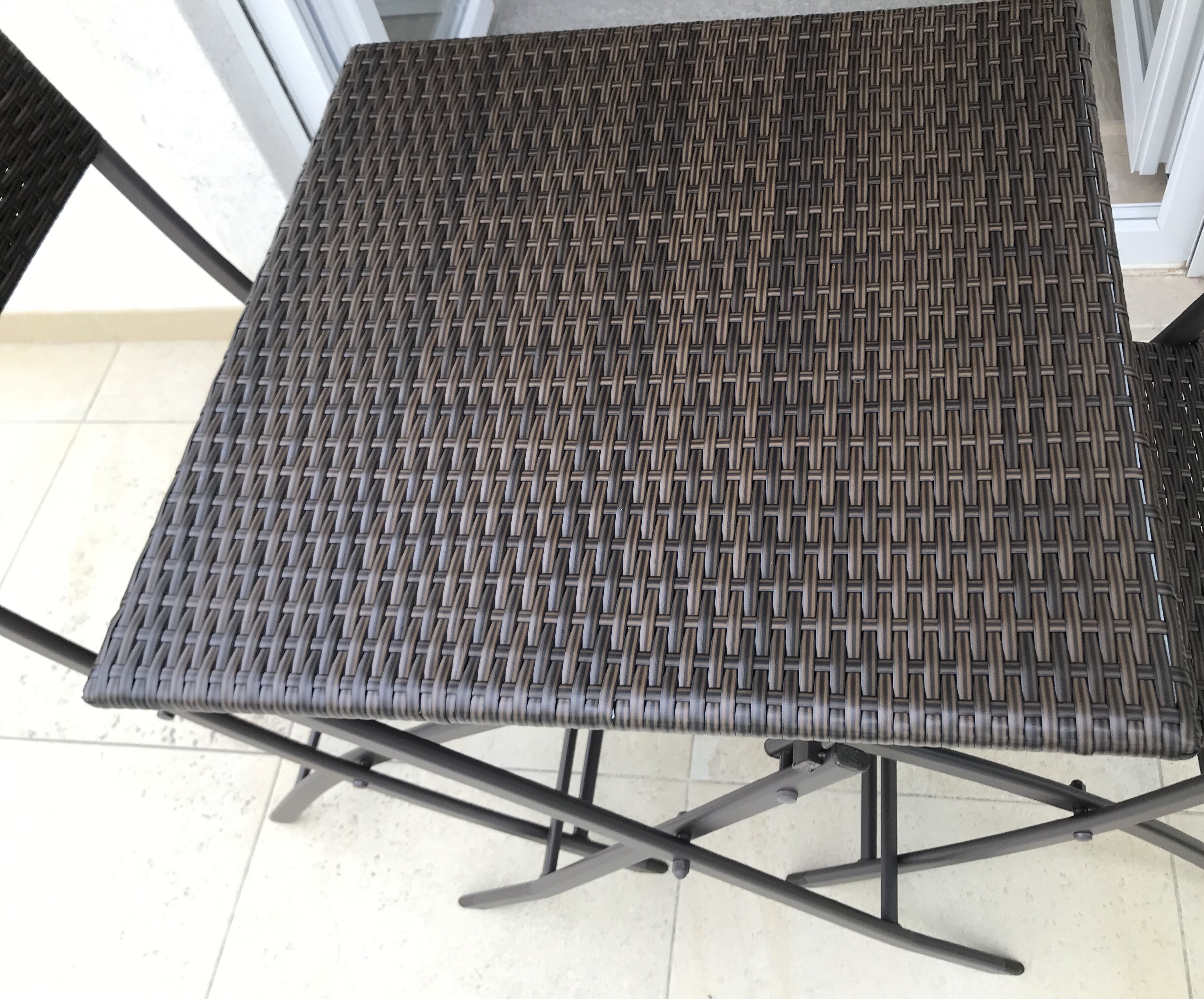 Une table carrée en métal, dotée d’un plateau en matériau tressé et d’un cadre pliable.