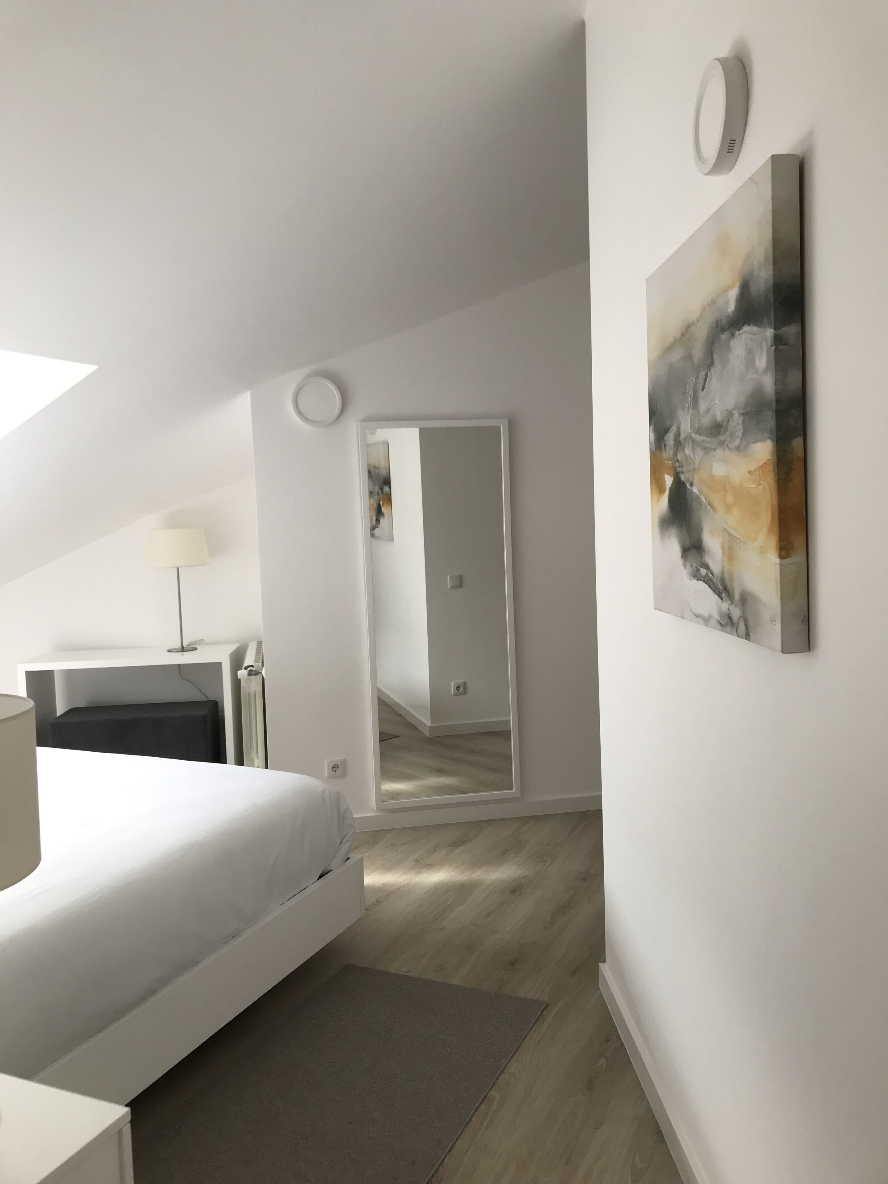 Una camera da letto moderna con un letto, un comodino, una lampada e un grande quadro astratto.
