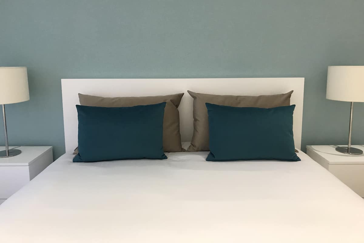 A bed with two pillows, a white headboard, and two bedside tables with lamps.
