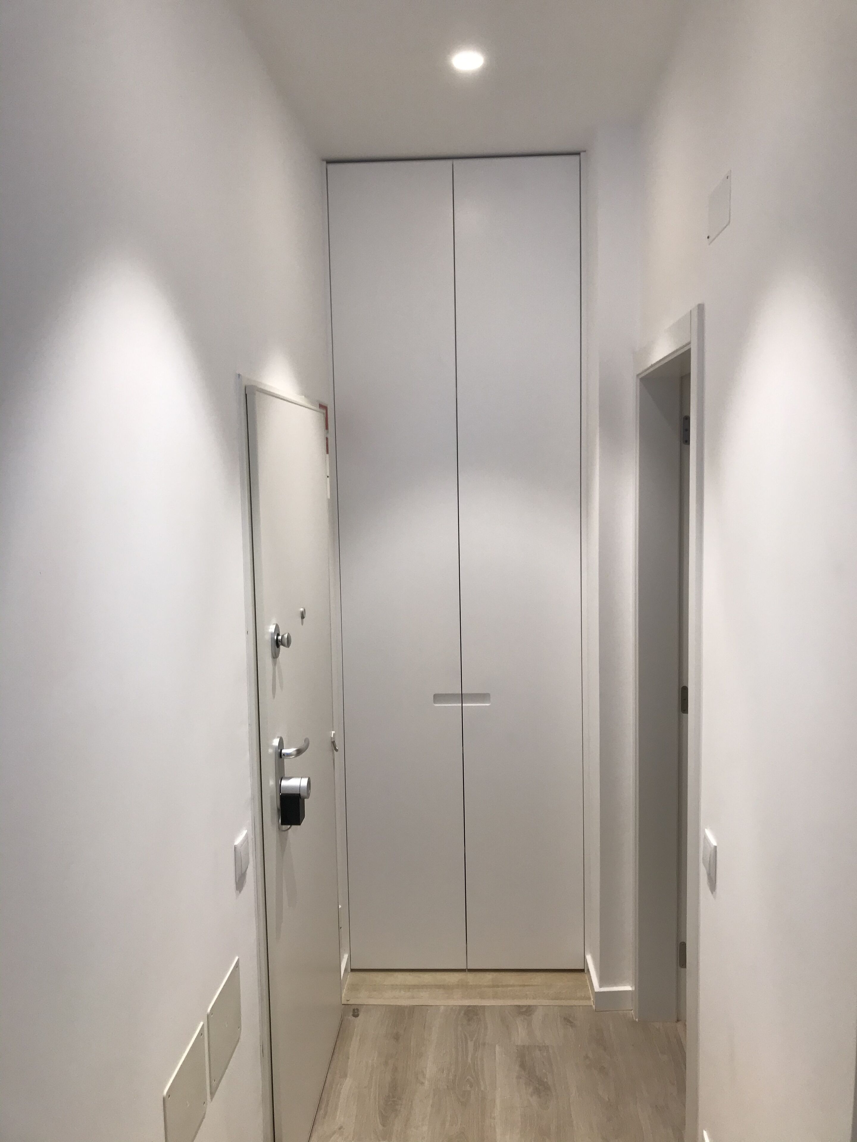 Un pasillo con una puerta doble, un picaporte y un interruptor de luz en la pared.