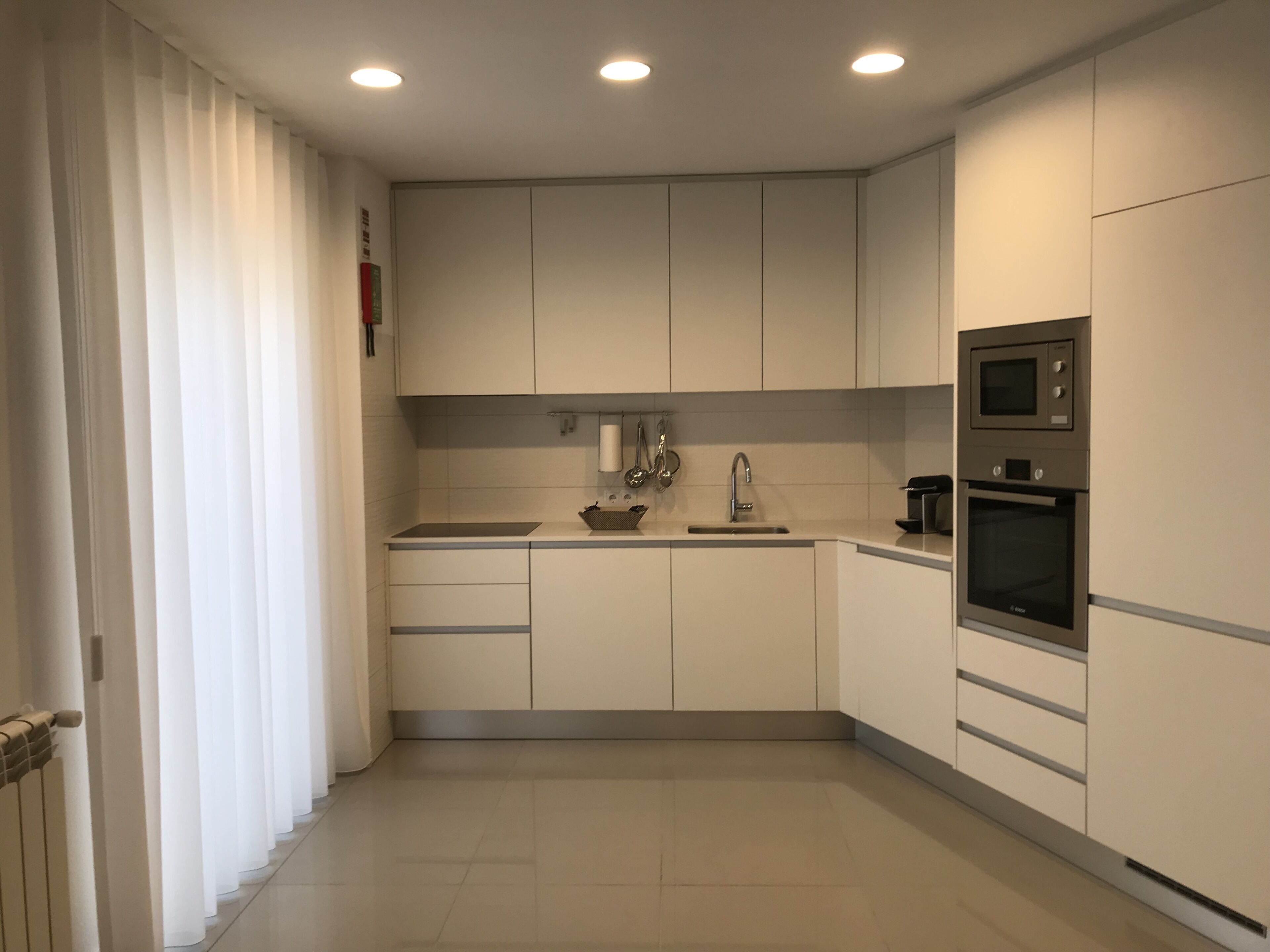 A modern kitchen with white cabinets, a sink, a microwave, and an oven.