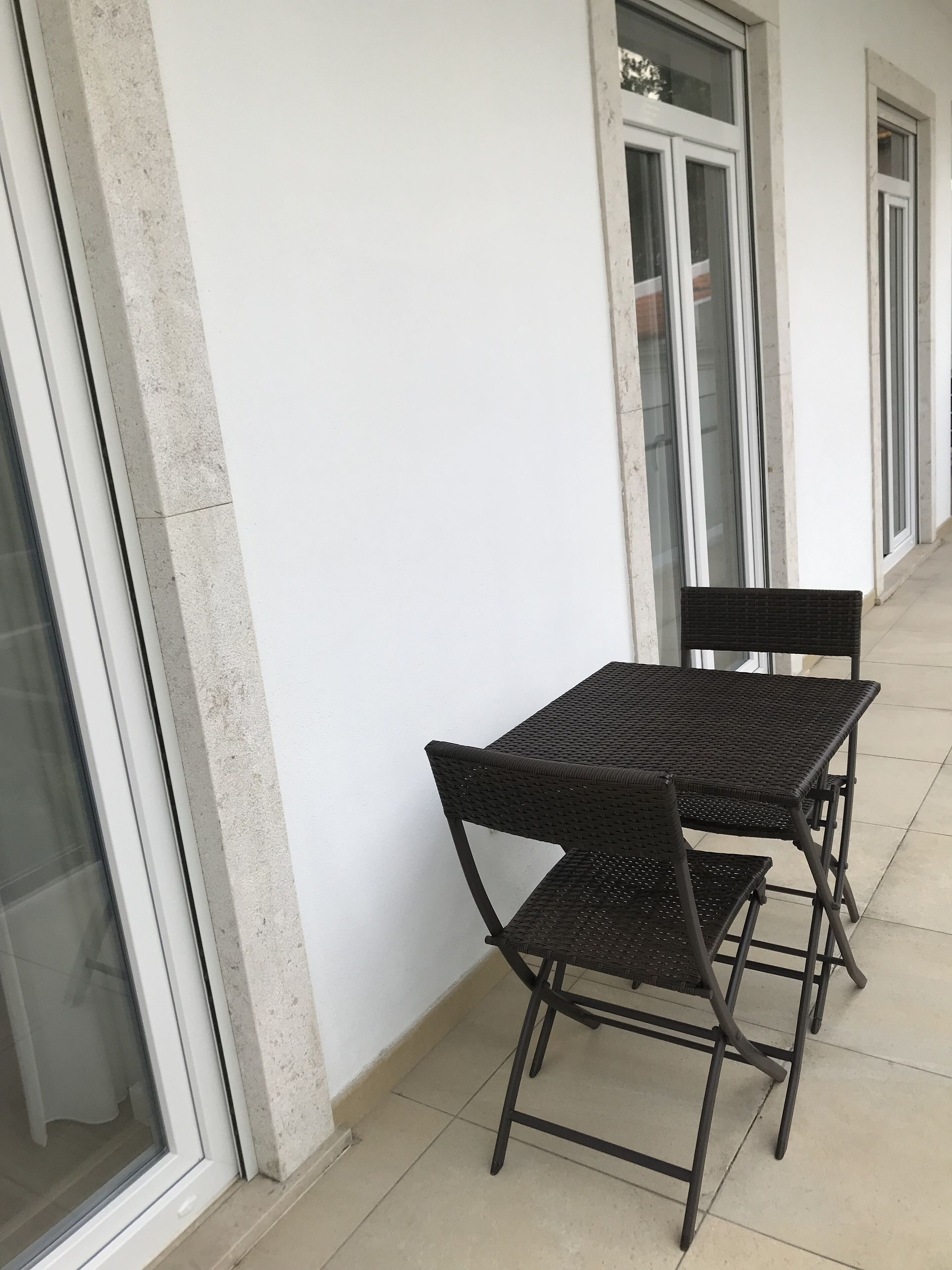 A small outdoor seating area with a table and chairs, adjacent to a building with large windows.