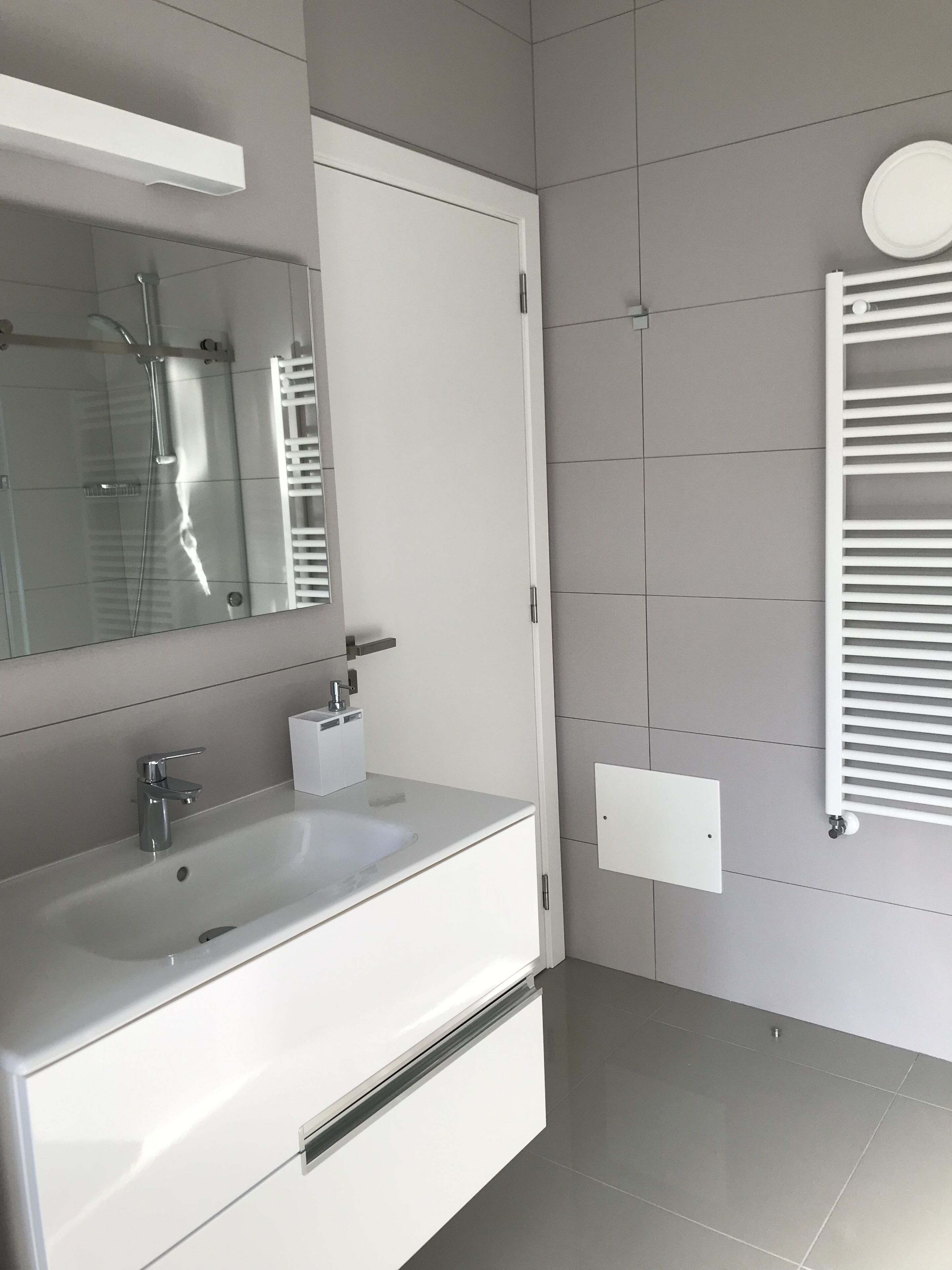 A modern bathroom with a white sink, mirror, and towel rack.