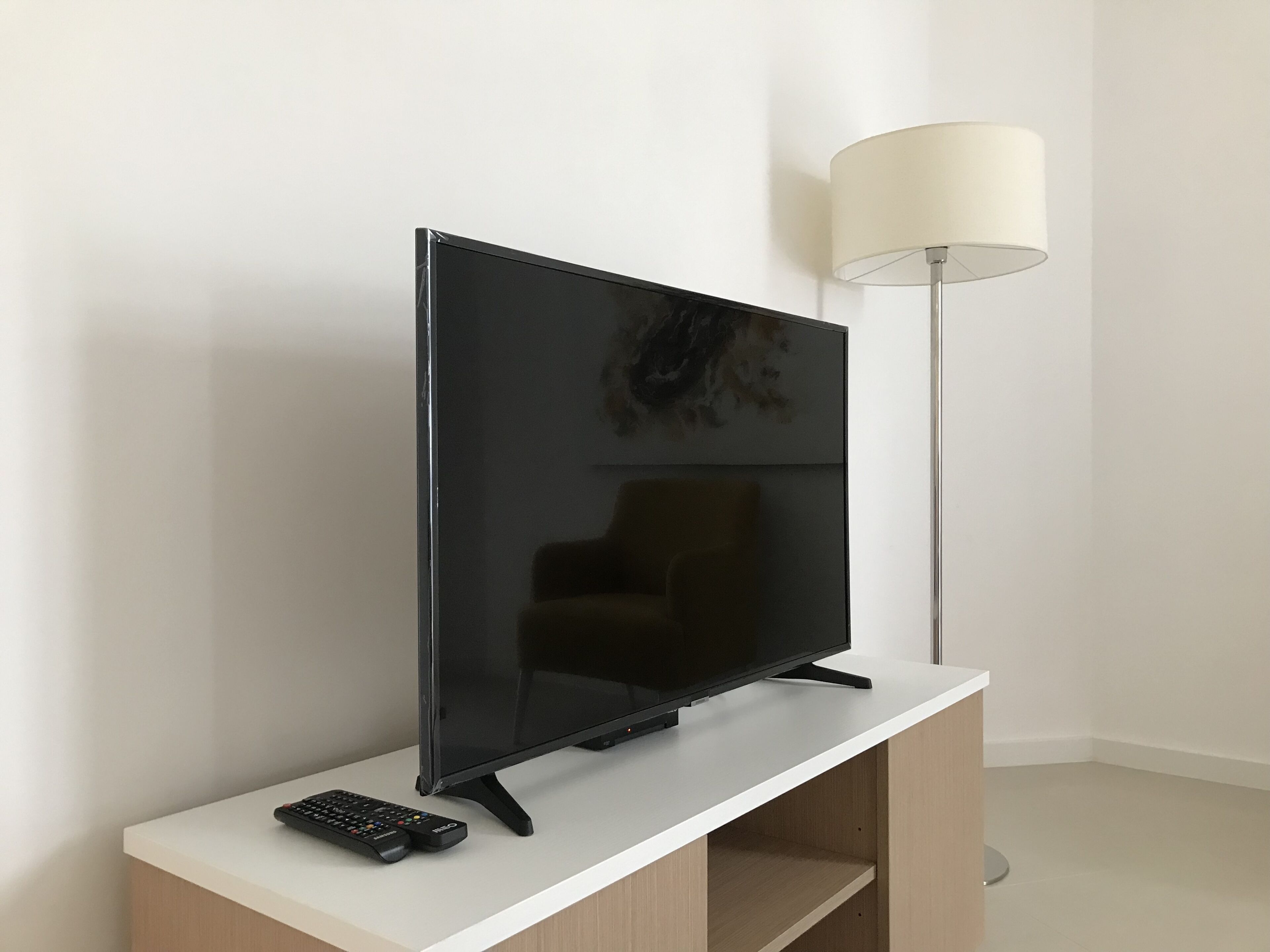 Un televisor de pantalla plana sobre un soporte blanco, con un control remoto a su lado.